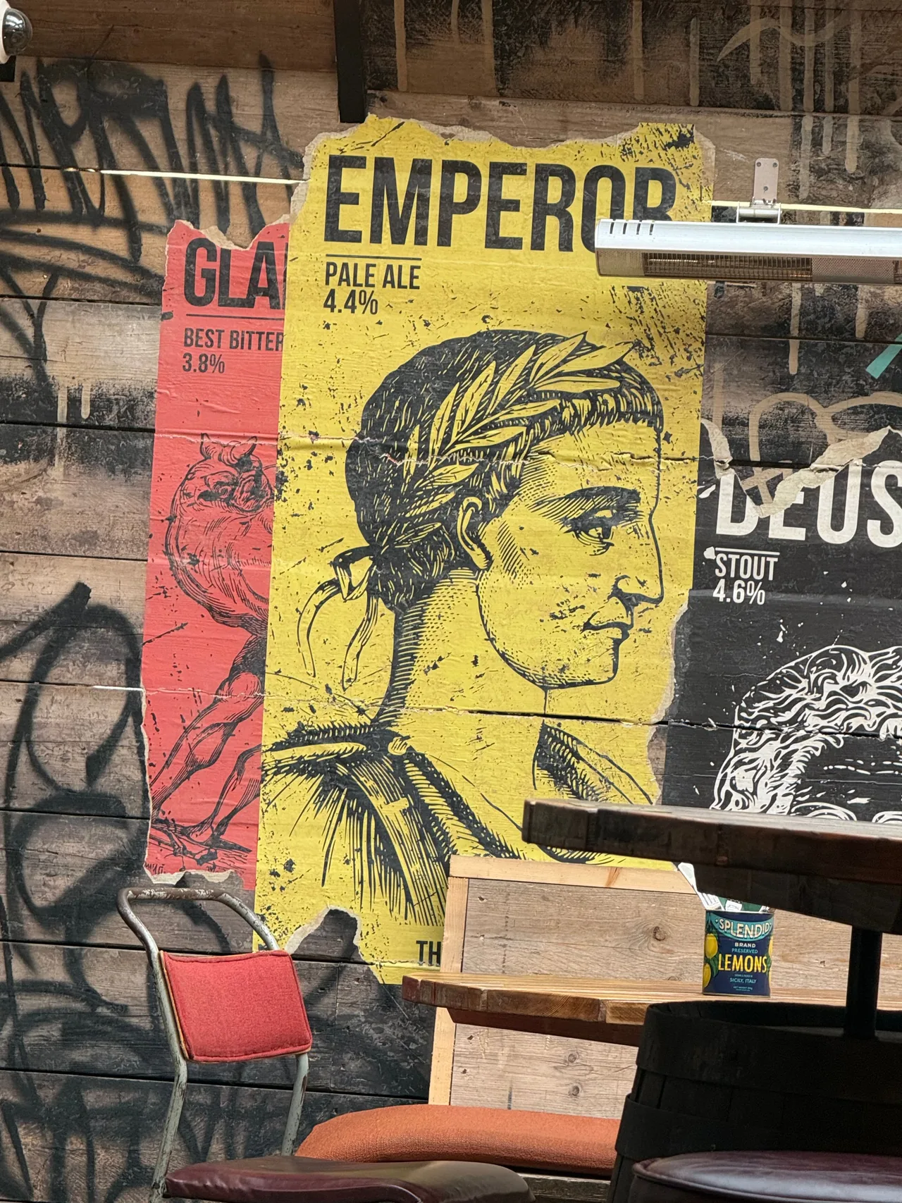 Um cartaz amarelo de Emperor Pale Ale 4,4% com um imperador romano em uma coroa de louros, em uma parede de madeira na Bath Brew House.