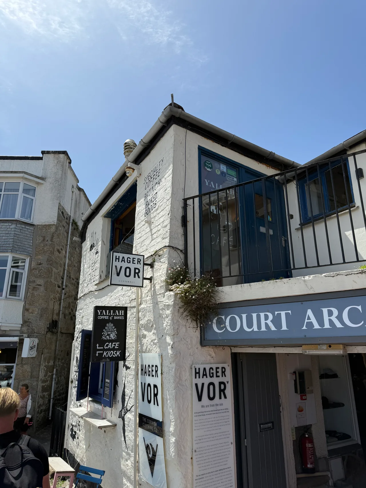 A white-and-blue corner building in St Ives housing Court Arcade and a row of small shops and a cafe kiosk.