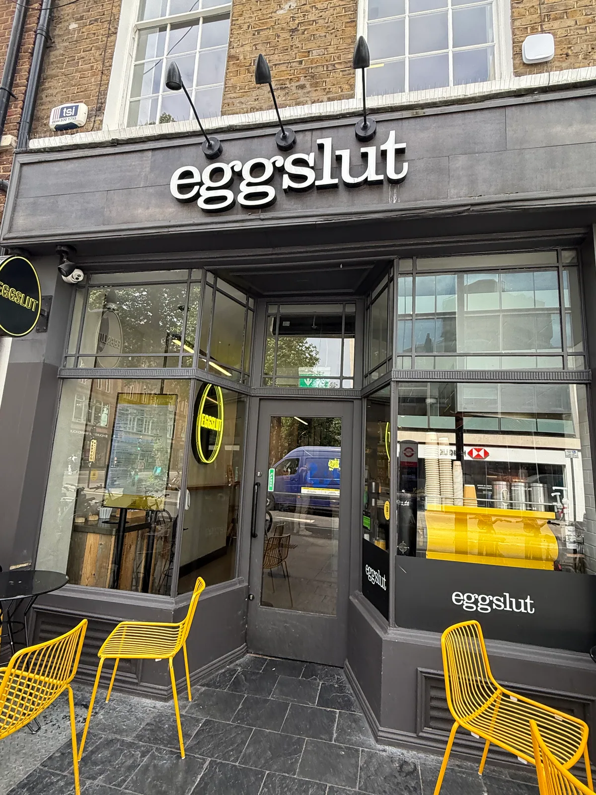 Eggslut Fitzrovia storefront at 19 Percy Street, dark facade with white eggslut signage and yellow chairs outside