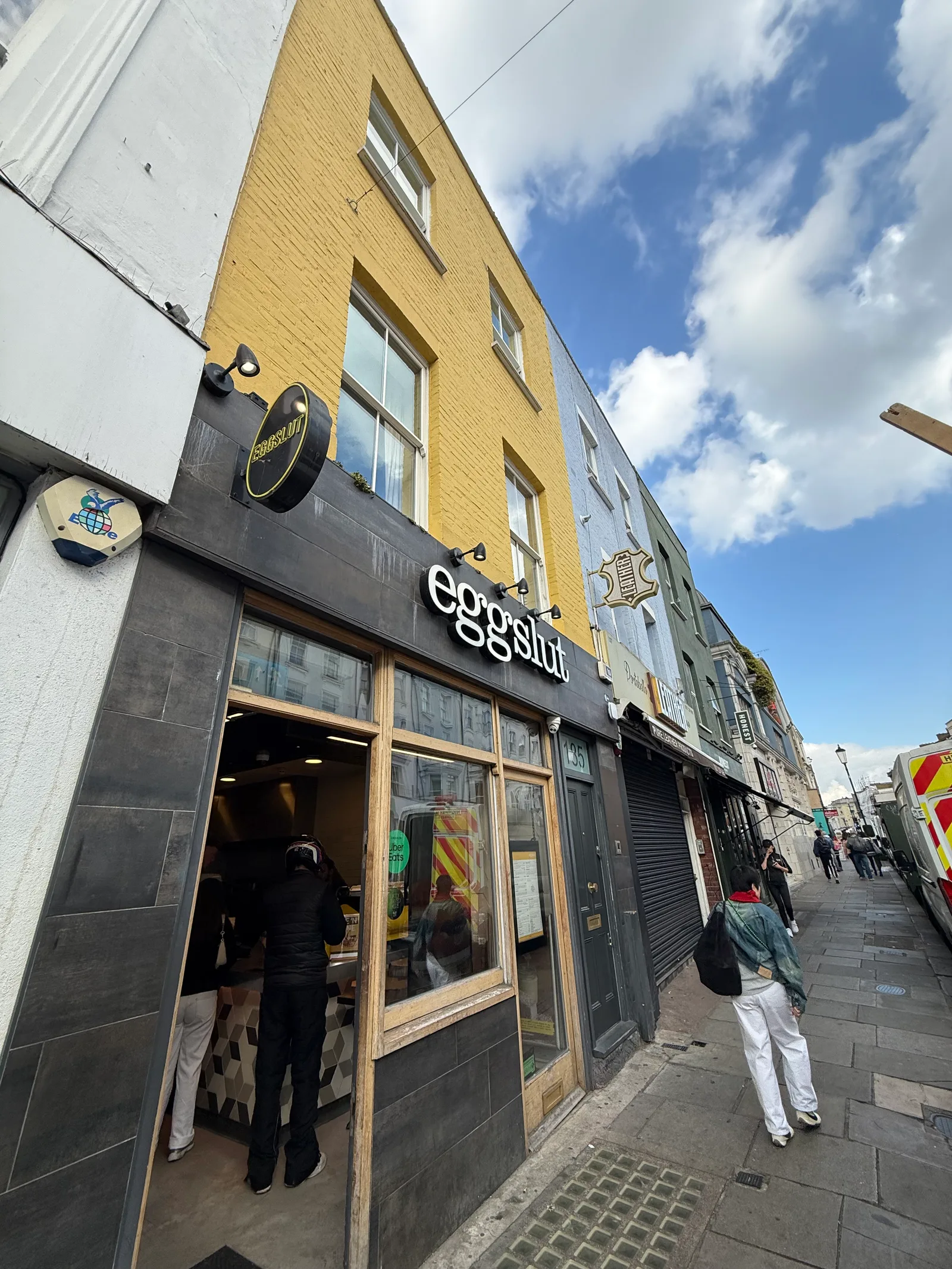 Eggslut Notting Hill — yellow-brick storefront on Portobello Road, customers inside, queue forming on a sunny weekend morning