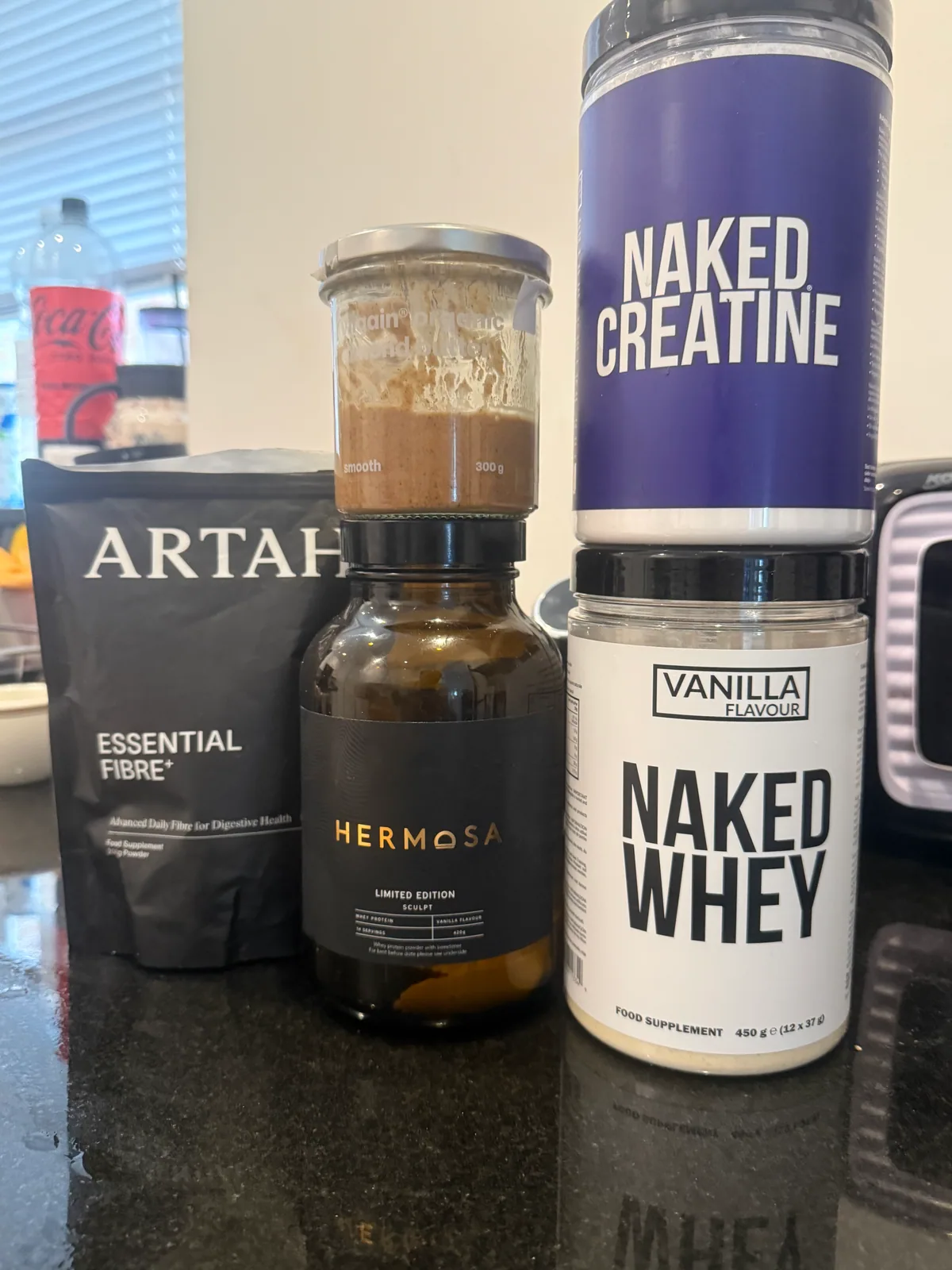 Naked Whey, Naked Creatine, Hermosa Sculpt protein, Artah Essential Fibre+ and Biona almond butter on a kitchen counter